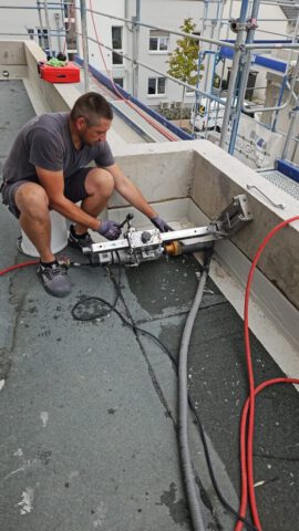 Mitarbeiter bei Kernbohrung auf Flachdach am Gerüst