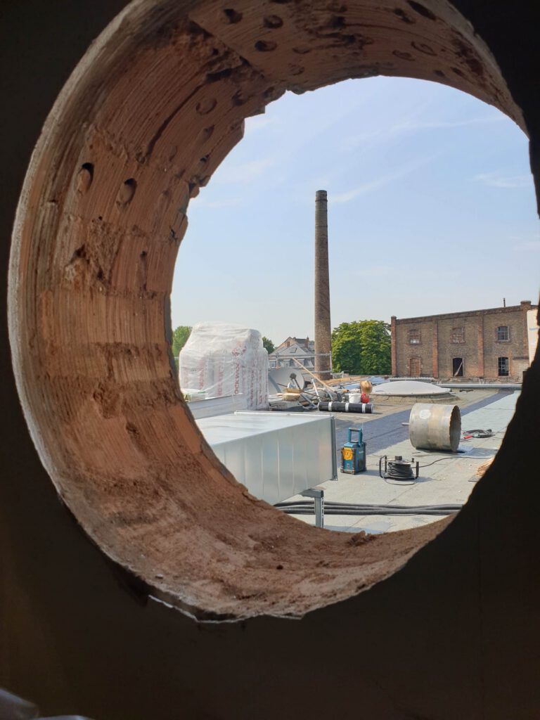 Blick durch Kernbohrloch auf Industriegelände mit Schornstein