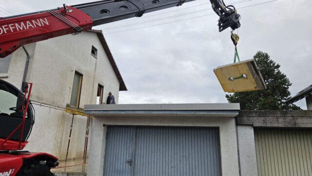Kran hebt herausgesägtes Betonstück eines Balkons von Garagendach