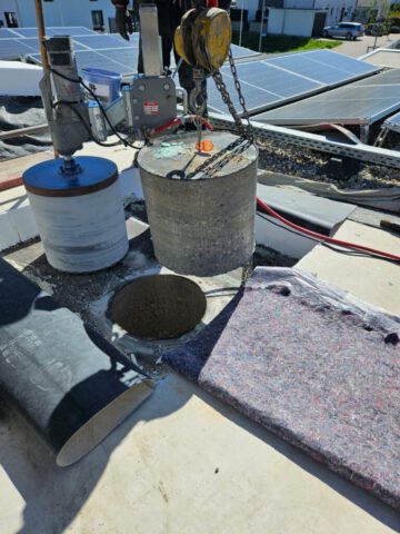 Großer Bohrkern wird mit Kran von Flachdach gehoben – Kernbohrung neben Solaranlage