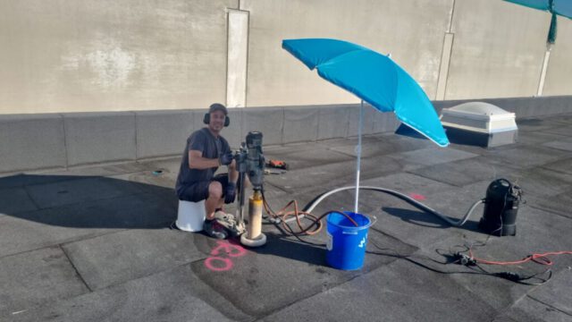Kernbohrung auf dem Dach im Hochsommer Mitarbeiter mit Kernbohrmaschine auf Flachdach bei Sonnenschein
